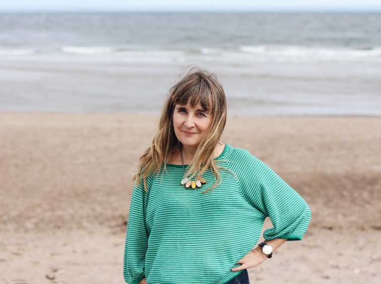 Illustrator Helen Stephens on a beach wearing a green jumper